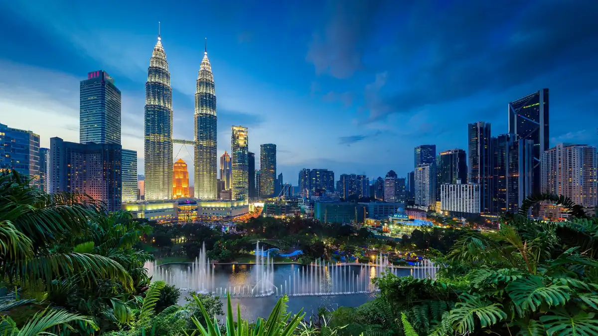 Petronas Twin Towers glowing at dusk above KLCC park in Kuala Lumpur