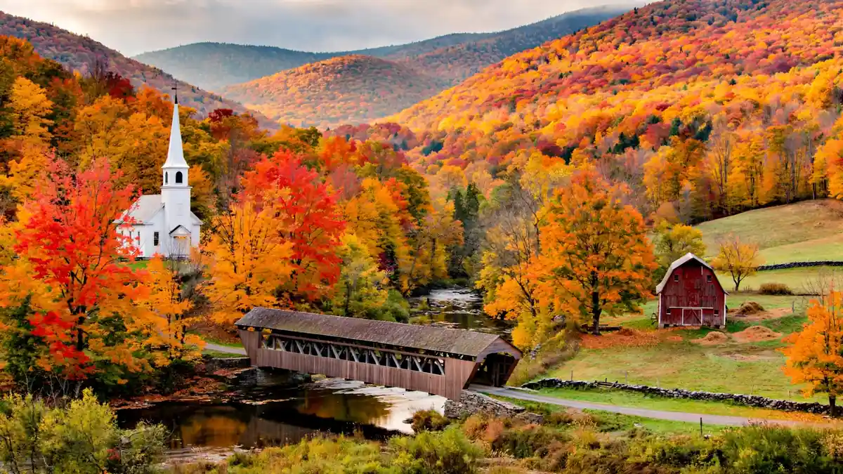 Vermont valley in peak fall foliage with a church steeple and covered bridge