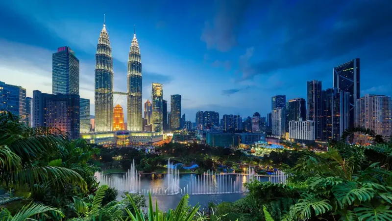 Petronas Twin Towers glowing at dusk above KLCC park in Kuala Lumpur